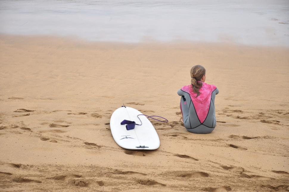 Free Image of Woman Sitting on Beach Next to Surfboard 