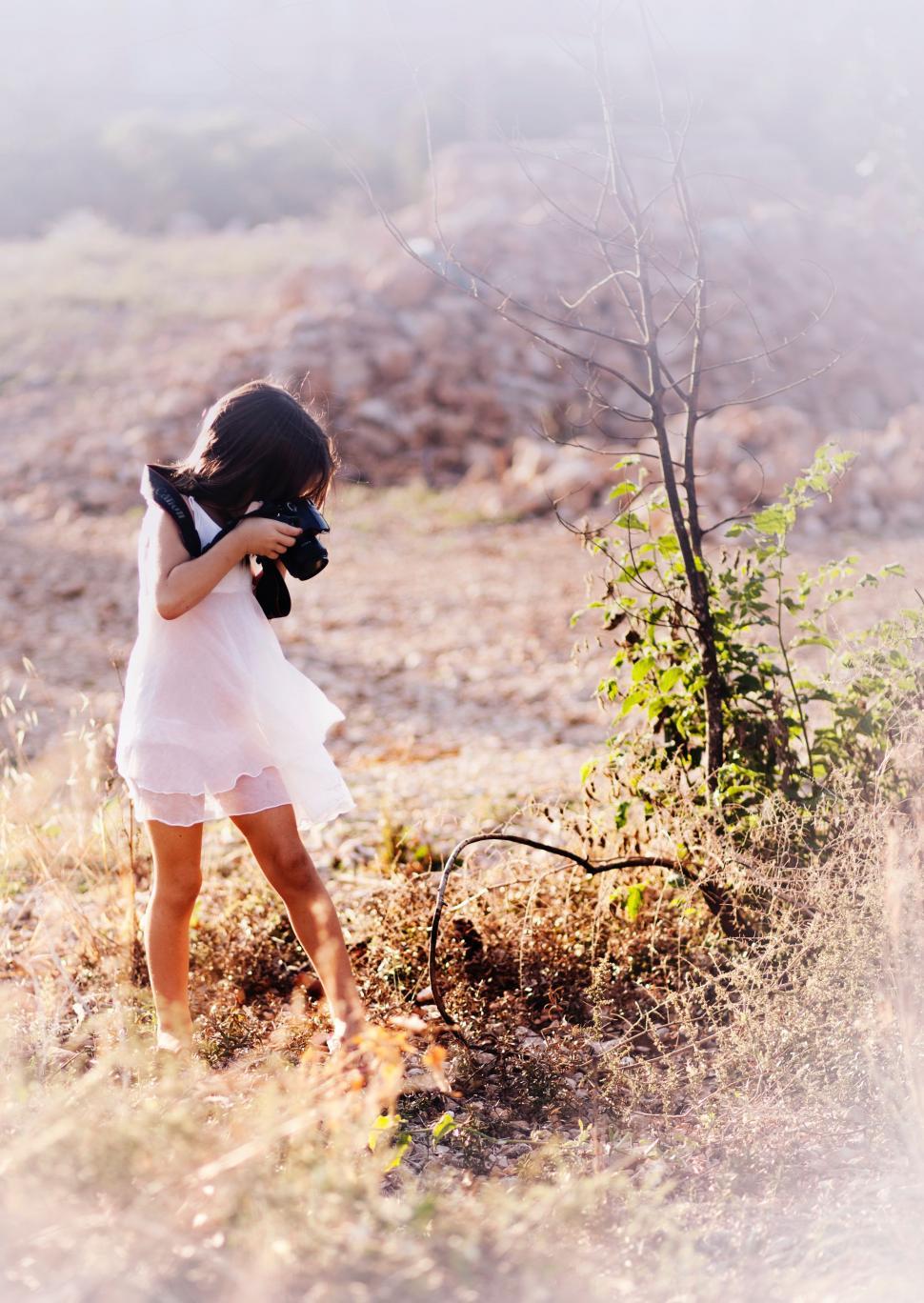 Free Image of Little Girl in White Dress Holding Camera 