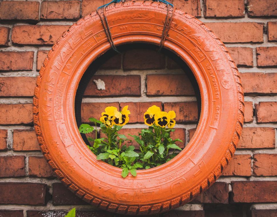 Free Image of Tire Hanging on Brick Wall With Flowers 