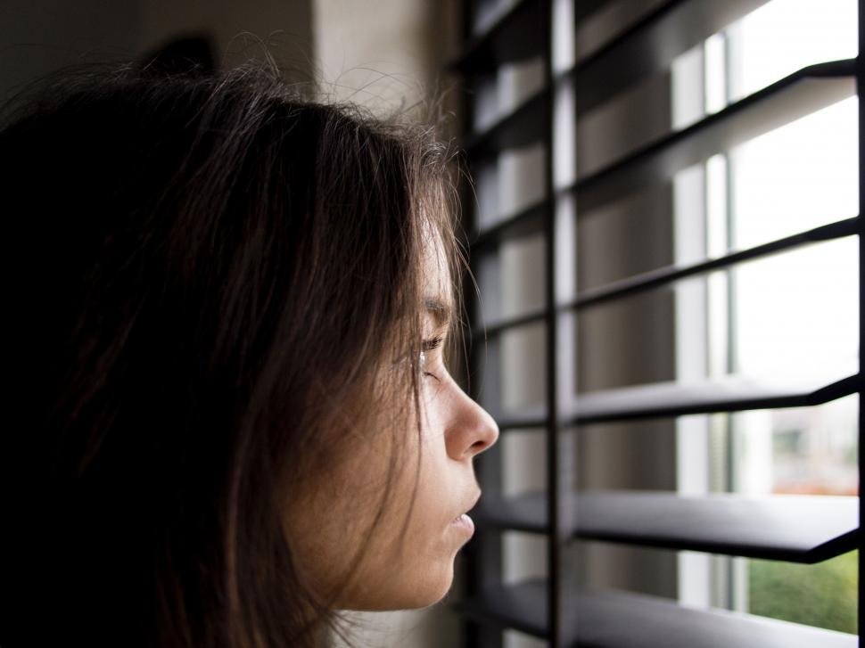 Free Image of Woman Looking Out of a Window With Blinds 