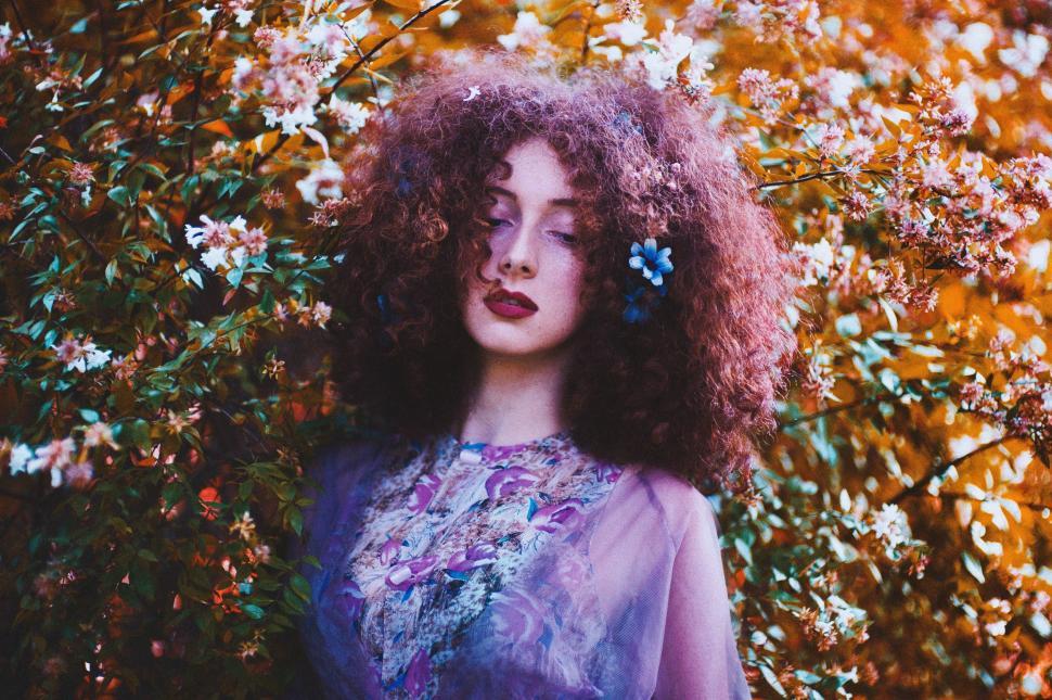 Free Image of Woman With Curly Hair Standing in Front of Flowers 