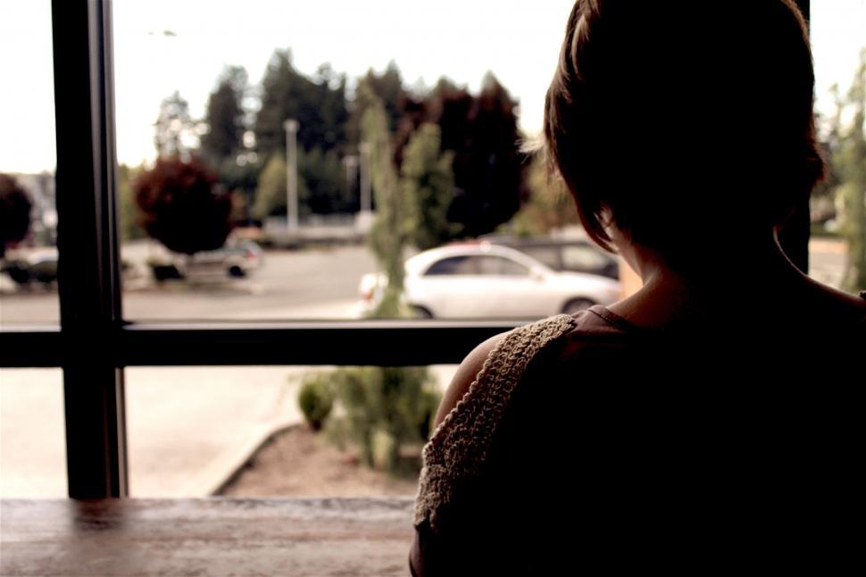 Free Image of Woman Looking Out a Window at a Parking Lot 