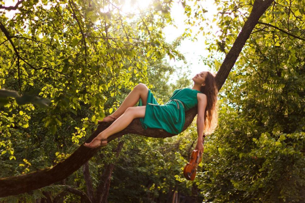 Free Image of Woman in Green Dress Sitting on Tree Branch 