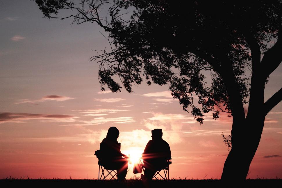 Free Image of Couple Sitting in Chairs Under Tree 