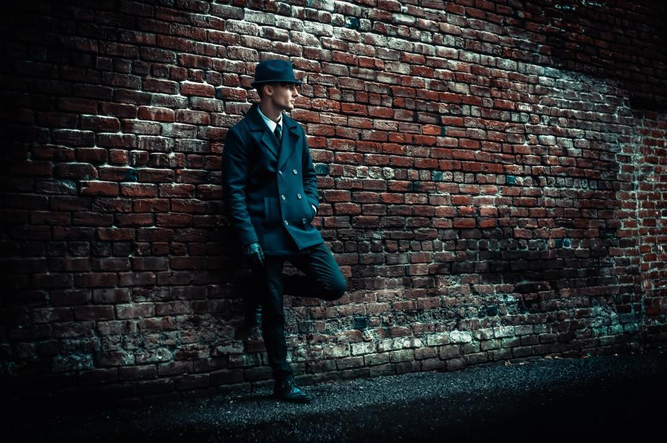 Free Image of Man Leaning Against Brick Wall With Hat 