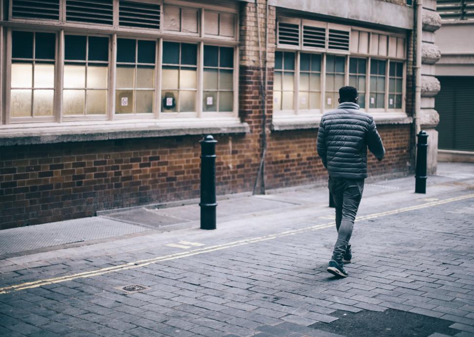 Free Image of Man Walking Down Street Next to Tall Building 