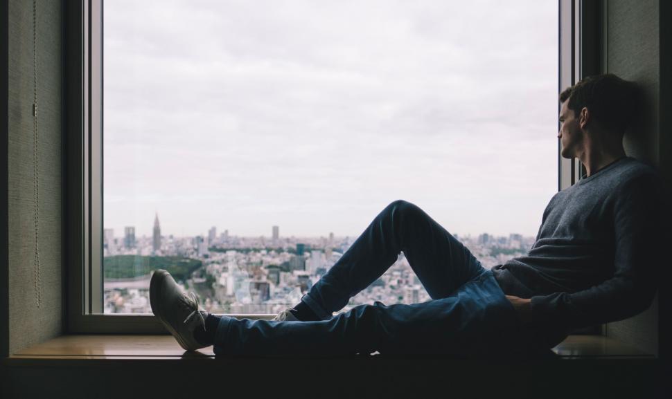 Free Image of Man Sitting on Window Sill Looking at City 