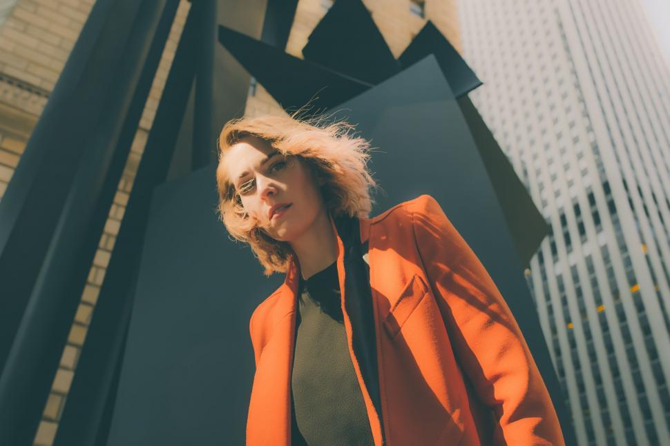 Free Image of Woman in Orange Jacket Standing in Front of Tall Building 