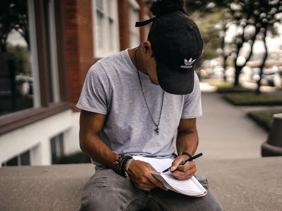 Free Image of Man Sitting on Ledge, Writing on Piece of Paper 