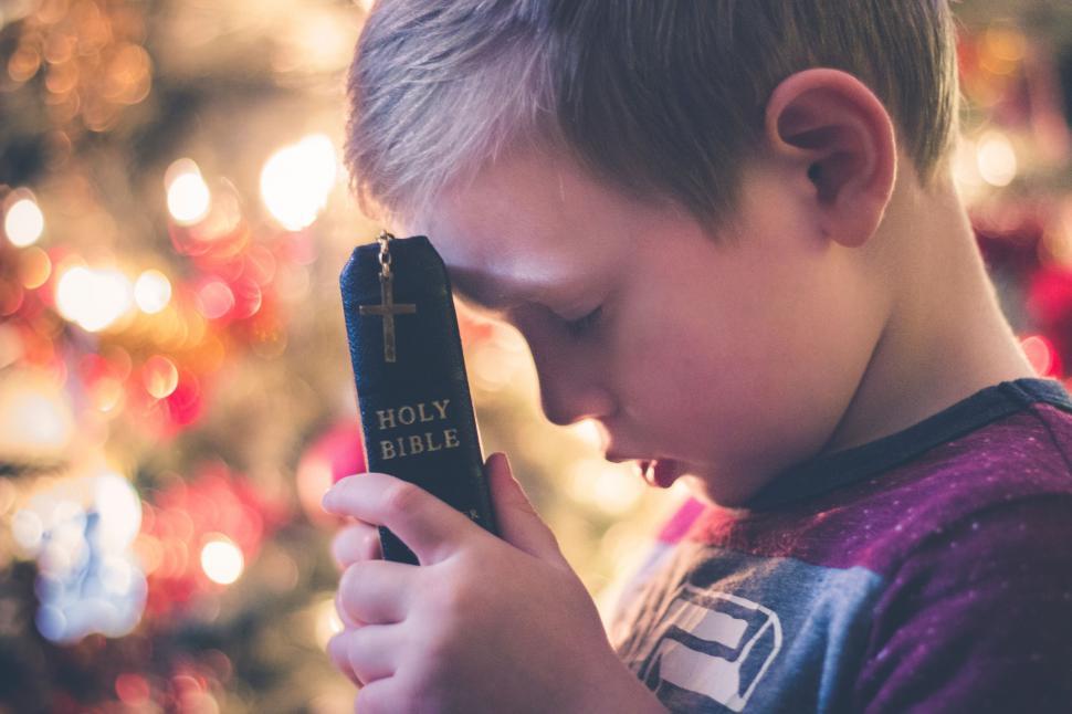 Free Image of Young Boy Holding Small Cross in Front of Christmas Tree 