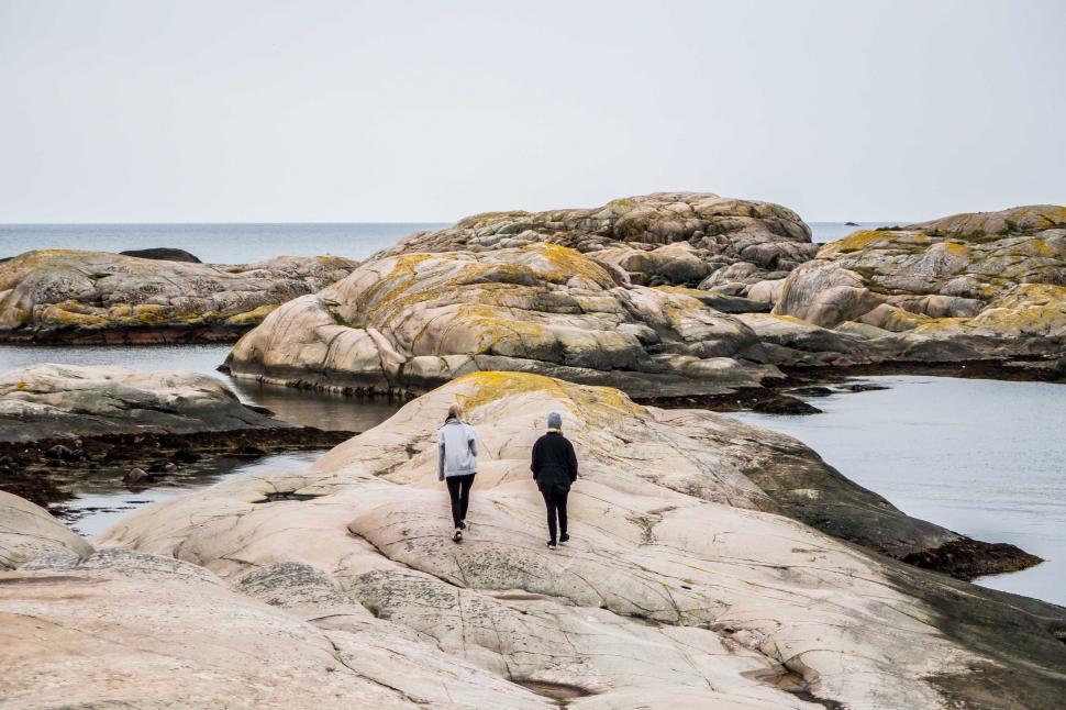 Free Image of Two People Walking on Rocks Near the Ocean 
