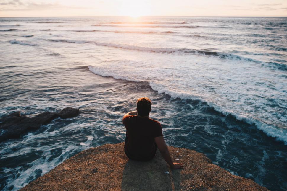 Free Image of Man Sitting on Cliff Overlooking Ocean 