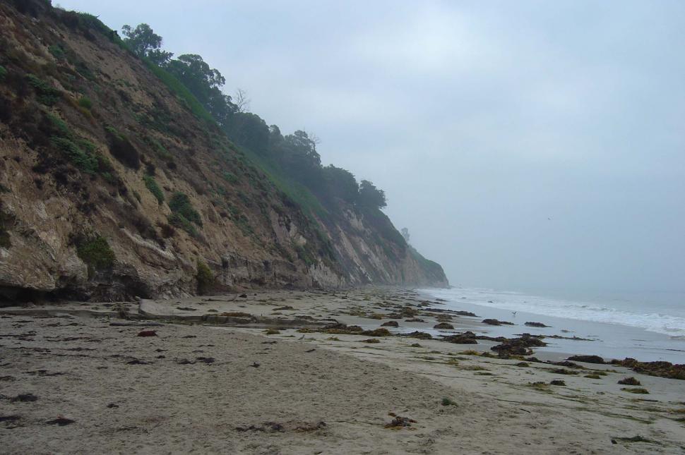 Free Image of Sandy Beach Next to Cliff on Cloudy Day 