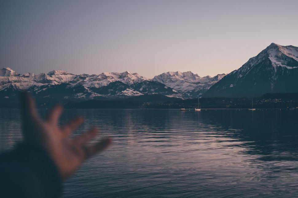 Free Image of Hand Reaching Out to Water With Mountains in Background 