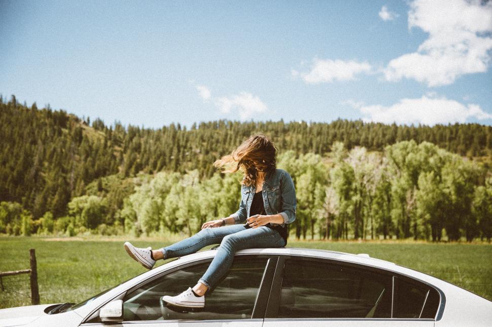 Free Image of Woman Sitting on the Hood of a Car 