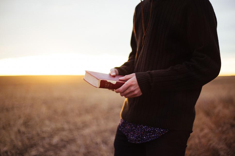 Free Image of Man Standing in Field Holding Book 