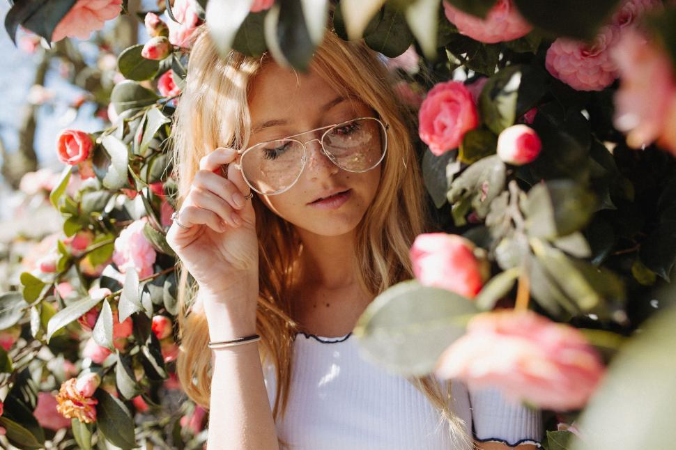 Free Image of Woman Wearing Glasses Standing in Front of Flowers 