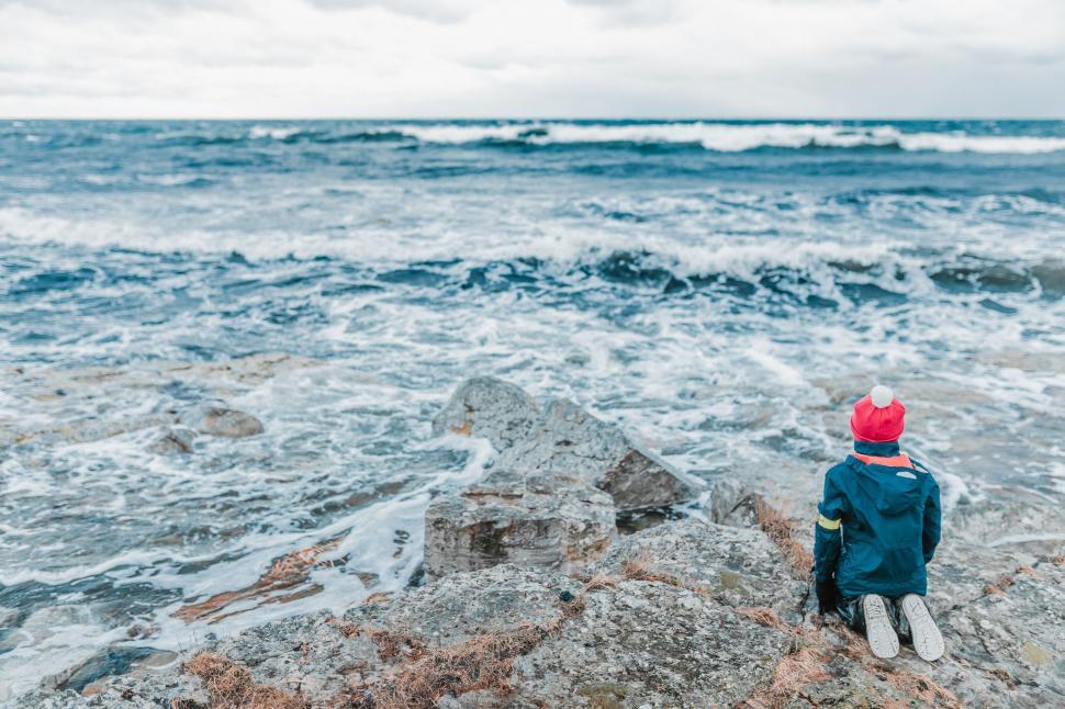 Free Image of Young Boy Sitting on Rock by Ocean 