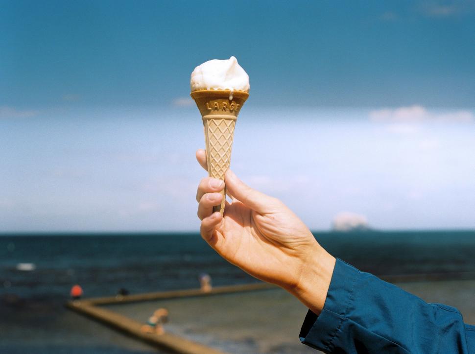 Free Image of Hand Holding Ice Cream Cone by the Ocean 