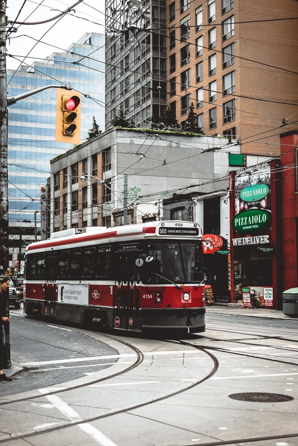 Free Image of Red and White Bus Driving Down Street Next to Tall Buildings 