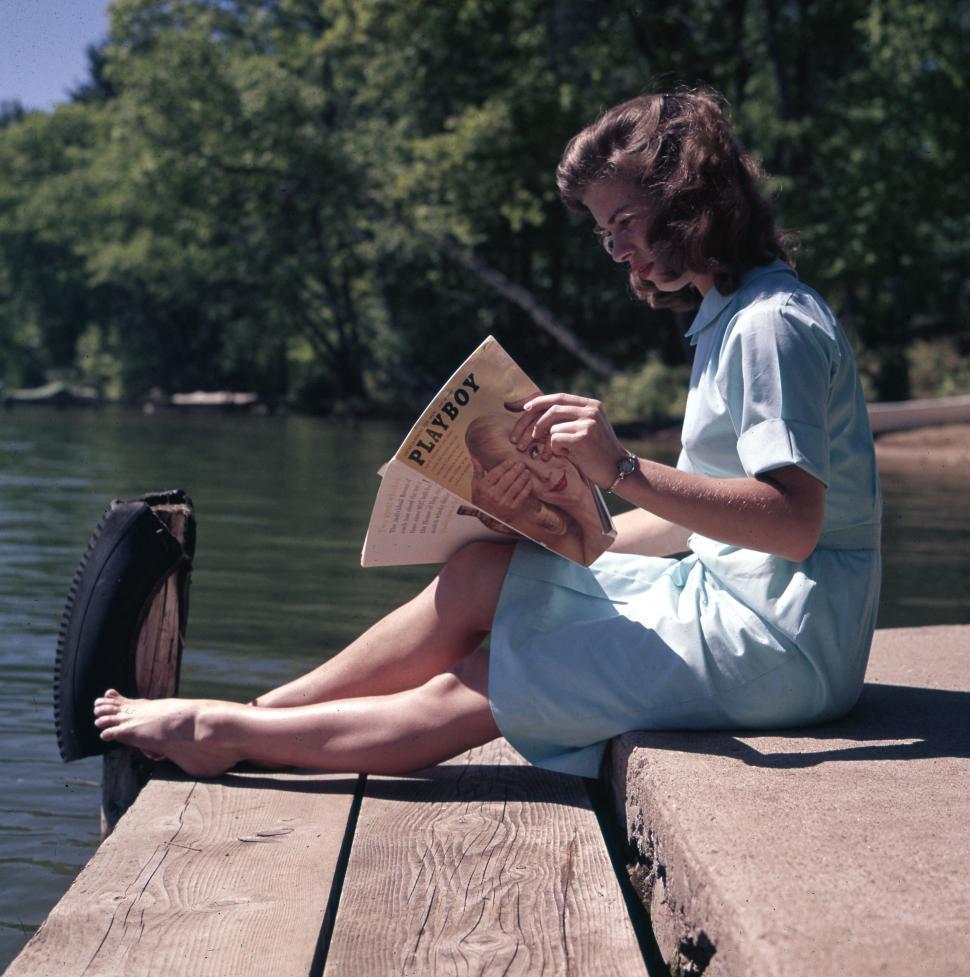 Free Image of Woman Sitting on Dock Reading Newspaper 