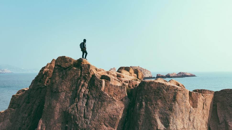 Free Image of Man Standing on Top of Large Rock by Ocean 