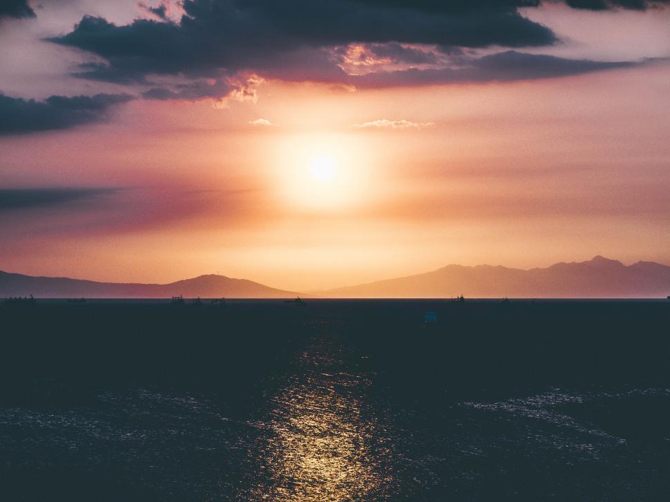 Free Image of Sun Setting Over Ocean With Mountains in Background 
