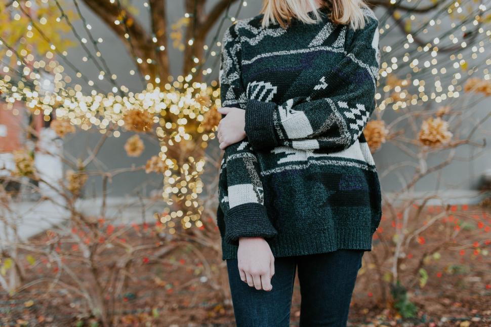 Free Image of Woman Standing in Front of Tree Wearing Black and White Sweater 