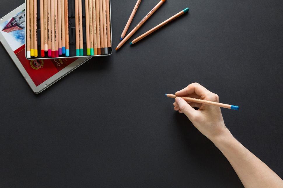 Free Image of Person Holding a Pencil Next to a Box of Colored Pencils 