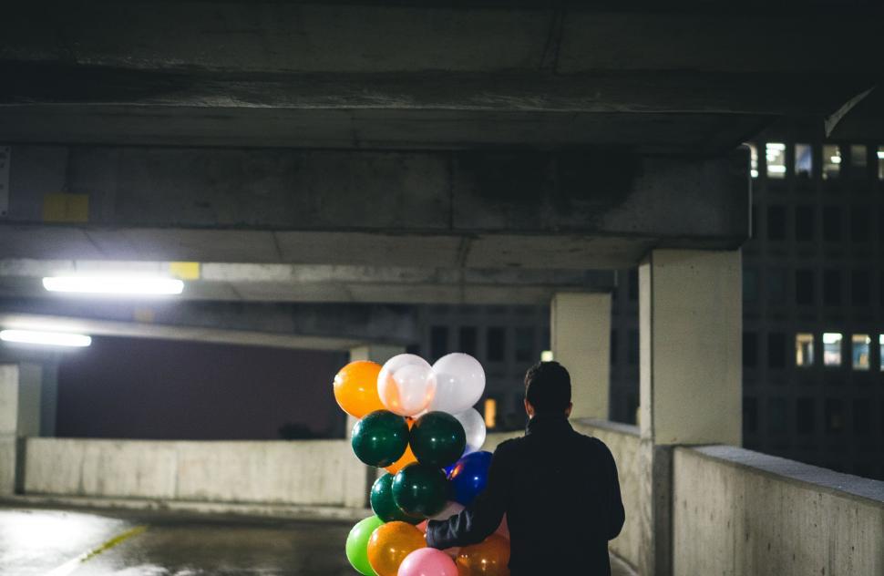 Free Image of Person Holding Bunch of Balloons in Parking Garage 