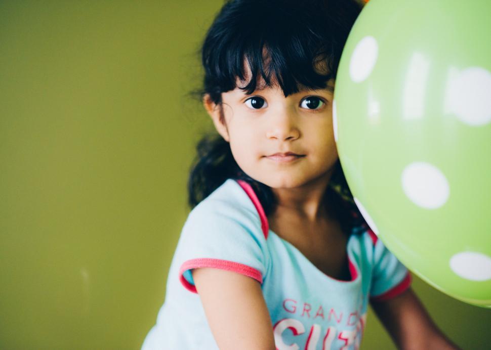 Free Image of Little Girl Holding Green Balloon in Front of Face 