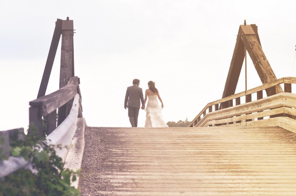 Free Image of Bride and Groom Walking Across a Wooden Bridge 