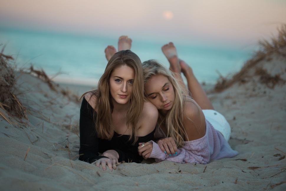 Free Image of Two Beautiful Young Women Relaxing on Sandy Beach 