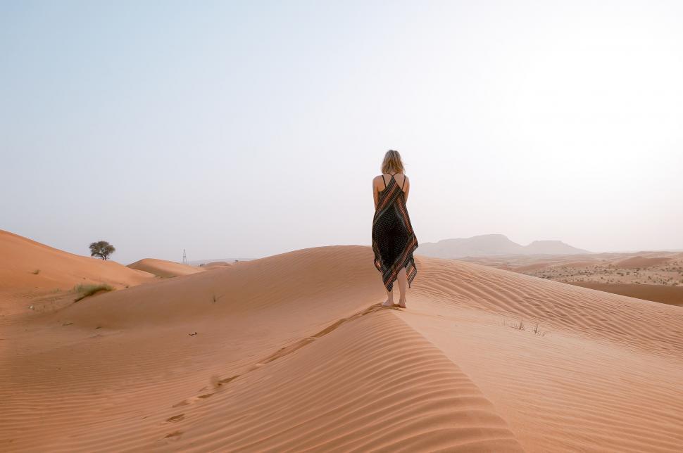 Free Image of Woman in a Black Dress Walking Across a Desert 