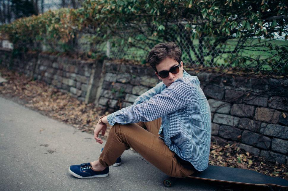 Free Image of Man Sitting on Skateboard by Roadside 