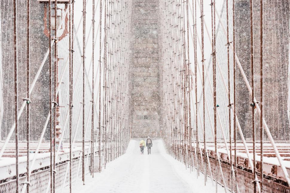 Free Image of Two People Walking Across a Bridge in the Snow 