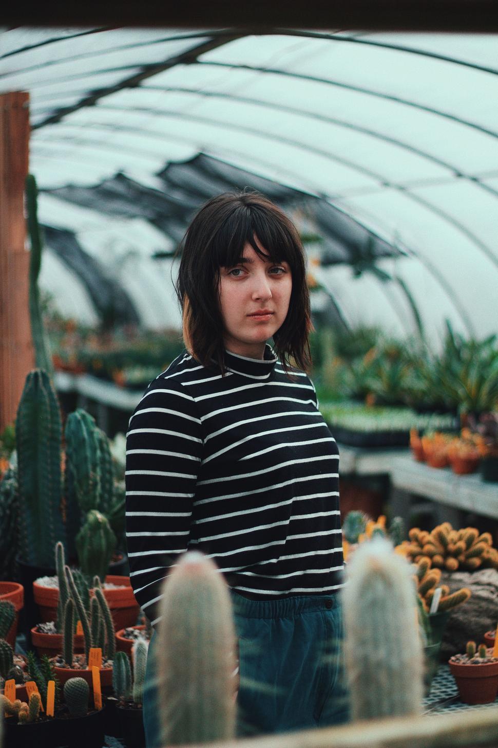 Free Image of Woman Standing in Front of Cacti-Filled Greenhouse 