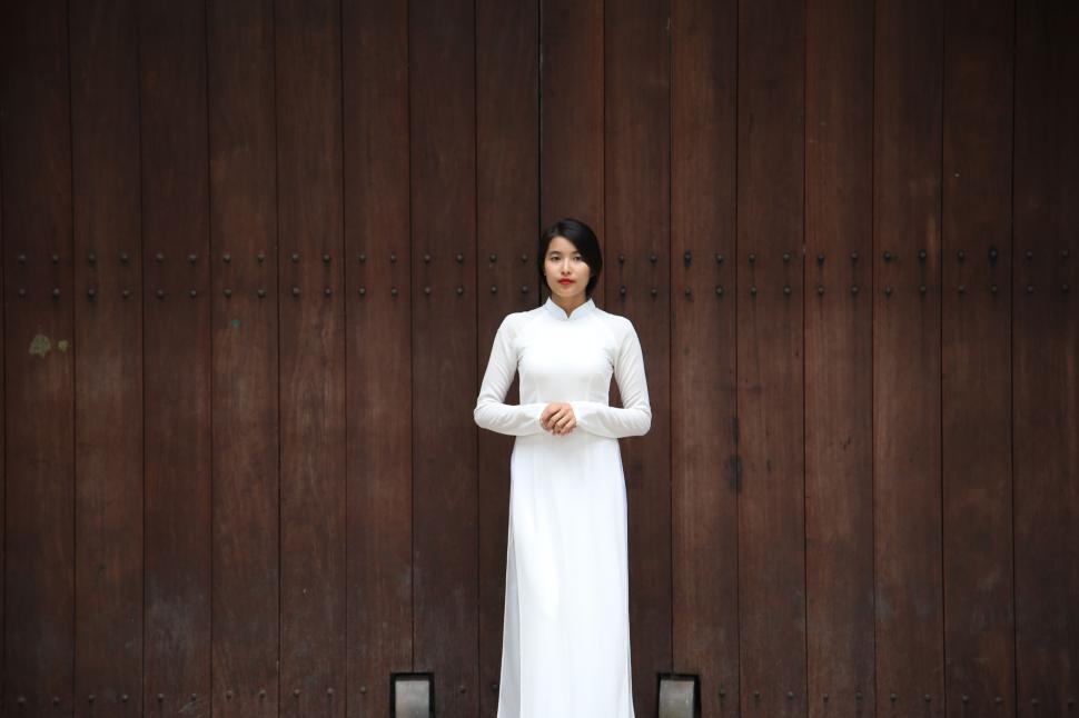 Free Image of Woman in White Dress Standing in Front of Wooden Wall 