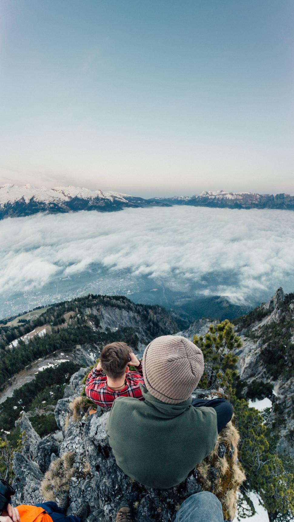 Free Image of Two People Sitting on a Mountain, Looking at Clouds 