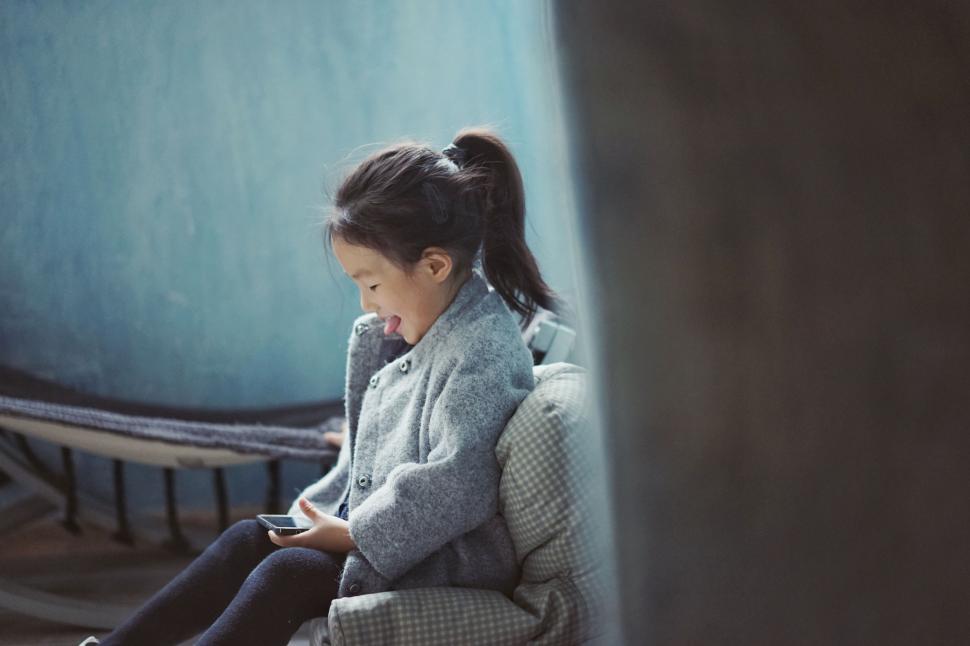 Free Image of Little Girl Sitting on Couch Looking at Cell Phone 