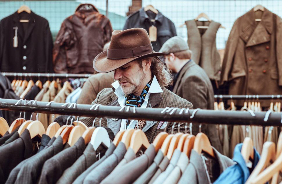 Free Image of Man in Hat Standing in Front of Clothes Rack 