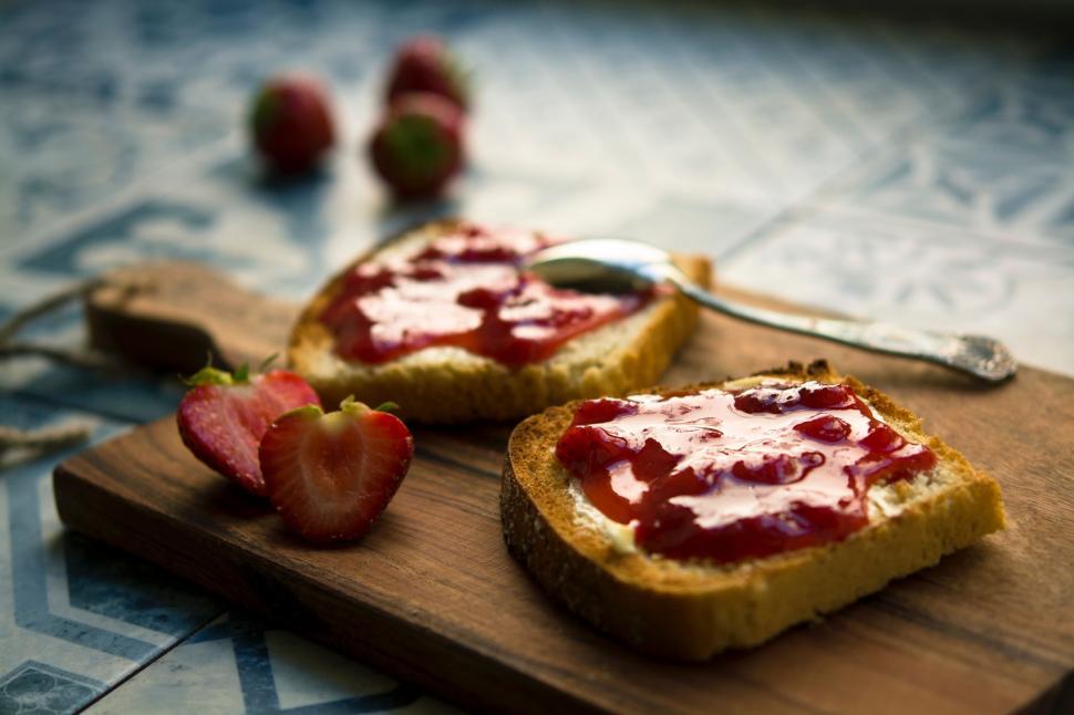 Free Image of Two Pieces of Bread With Jam and Strawberries on a Cutting Board 