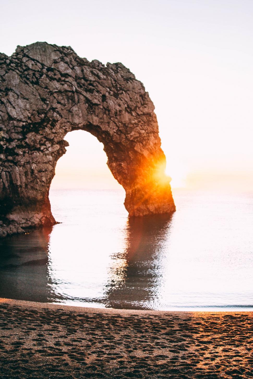 Free Image of Sun Setting Behind Rock Formation on Beach 