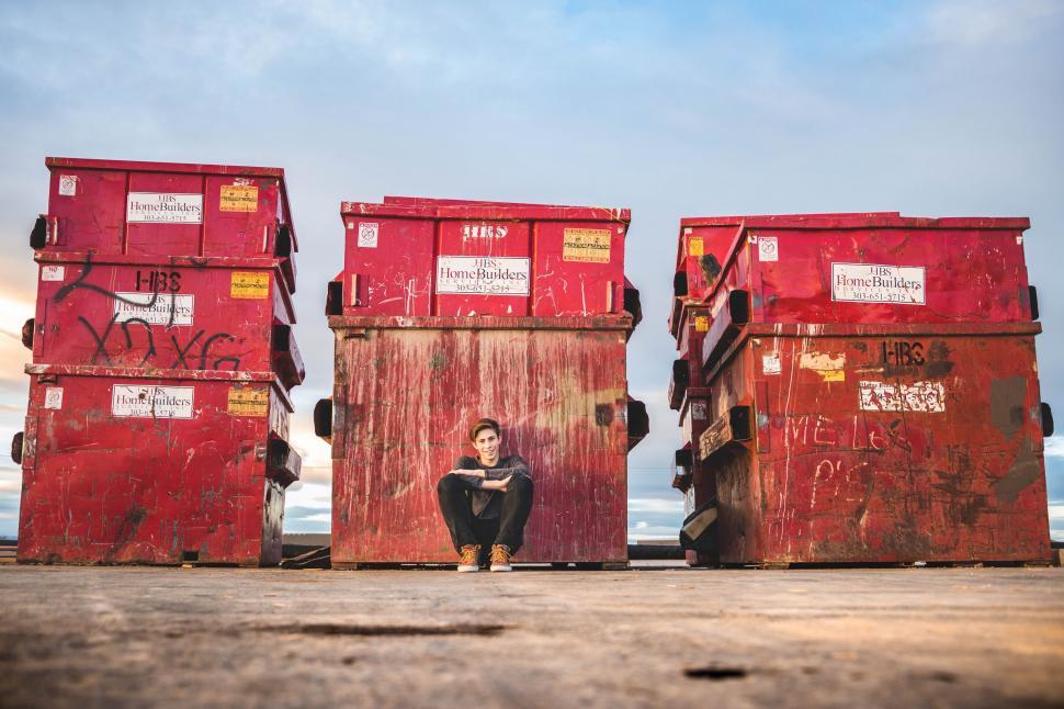 Free Image of Woman Sitting in Front of a Stack of Red Trash Cans 