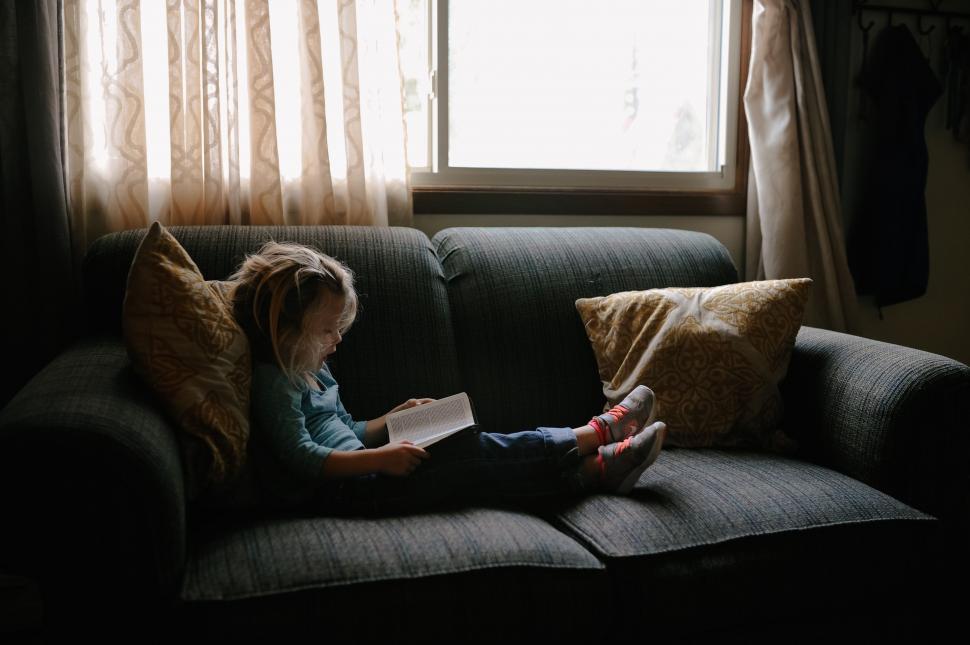 Free Image of Little Girl Reading Book on Couch 