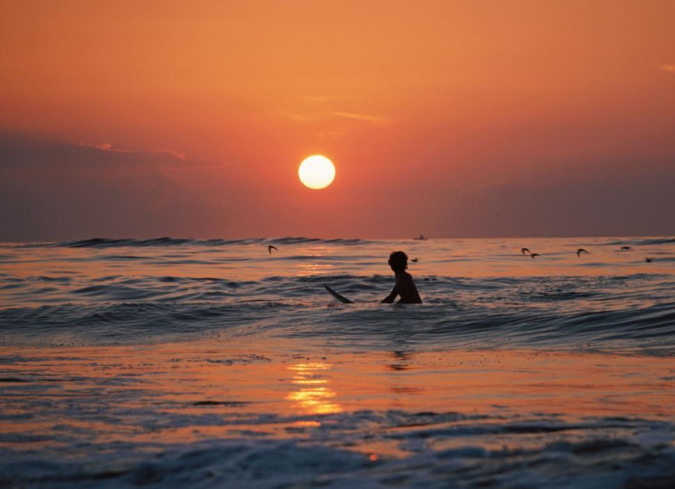 Free Image of Person Riding Surf Board in Ocean at Sunset 