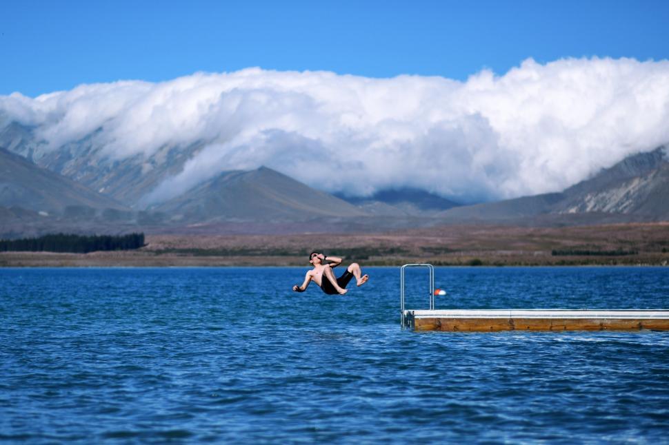 Free Image of Man Jumping Into Body of Water With Mountains in Background 