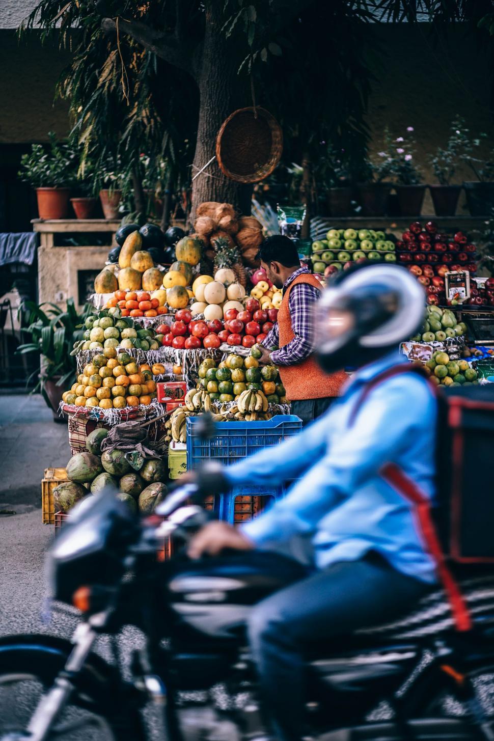 Free Image of Man Riding Motorcycle Past Fruit Stand 