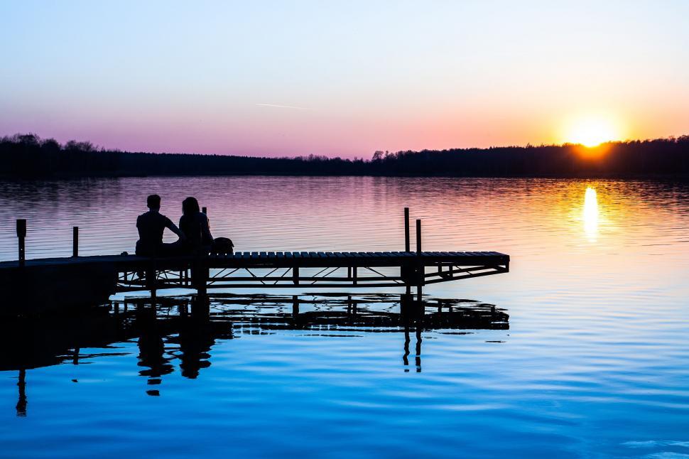 Free Image of Two People Sitting on a Dock Watching the Sun Set 