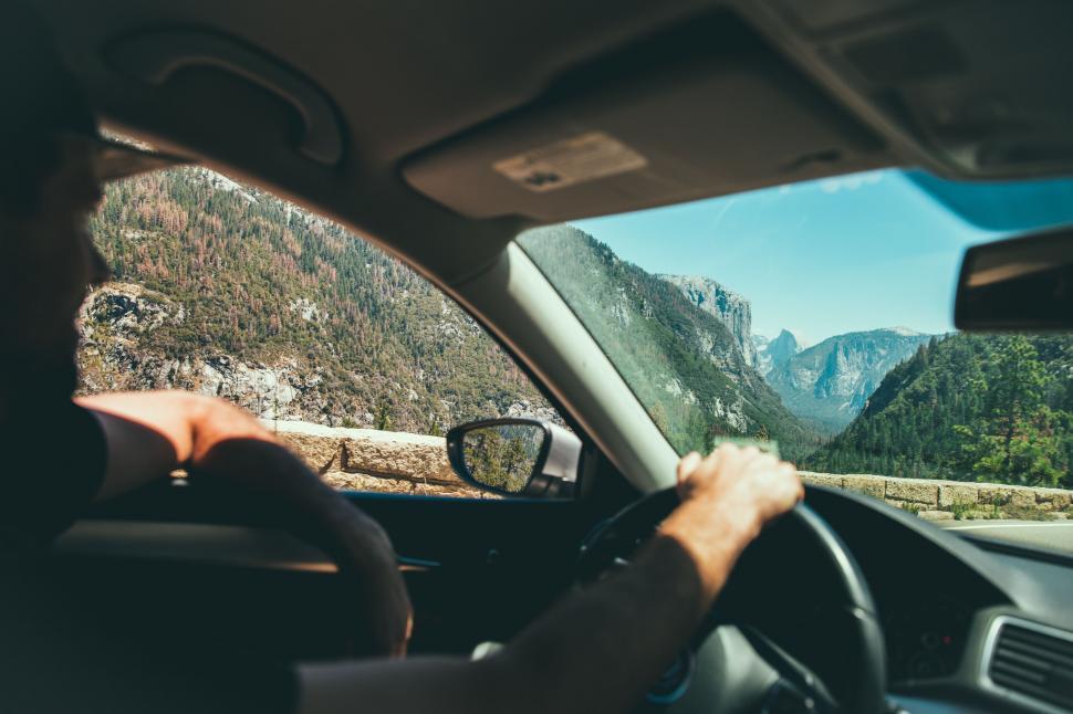 Free Image of Man Driving Car on Road With Mountains in Background 